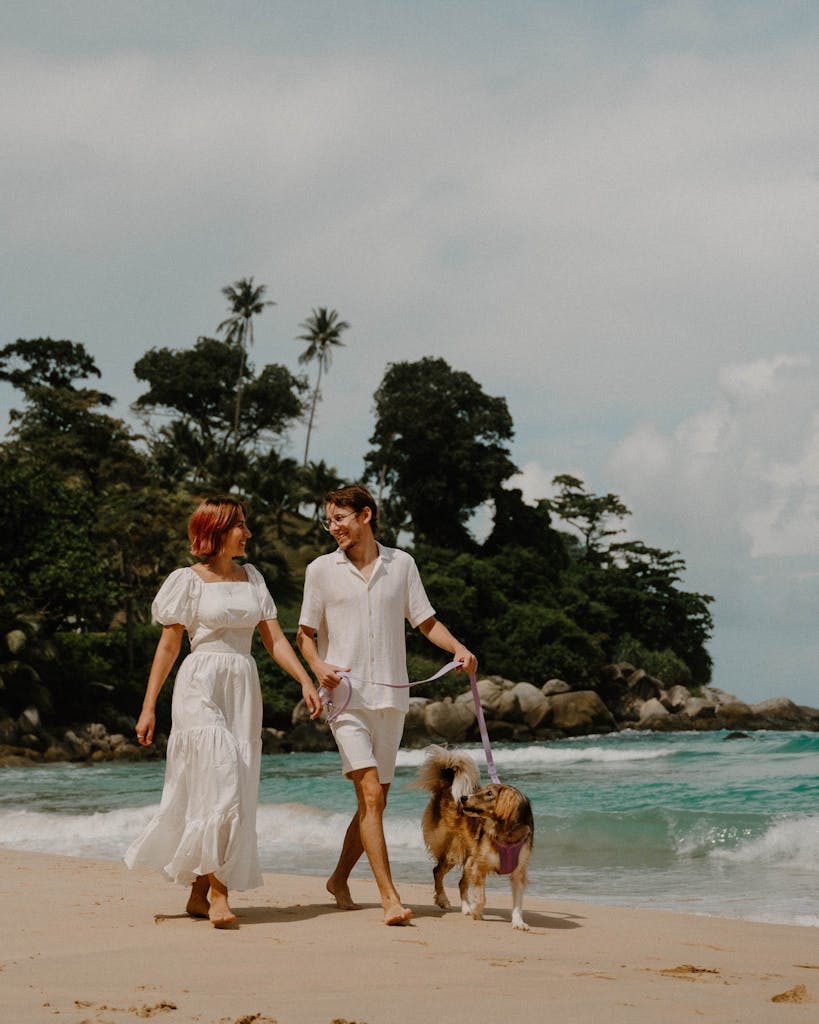 A couple walks their Australian Shepherd on a tropical beach in Phuket, Thailand.