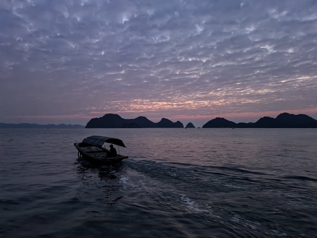 A lone boat sails at twilight in Halong Bay against a dramatic sky.