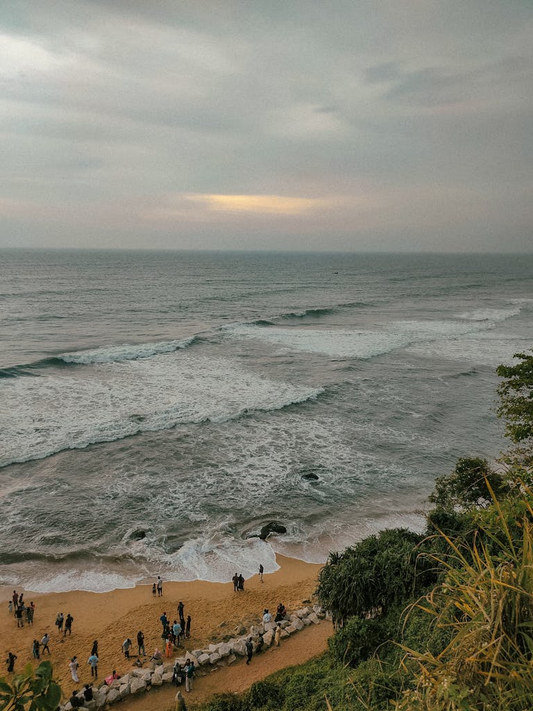 A scenic view of Varkala Beach with people enjoying the calm waves under an overcast sky.