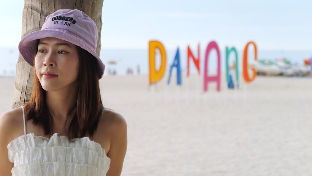 A woman in a bucket hat enjoying a sunny day at Danang beach with colorful signs in the background.