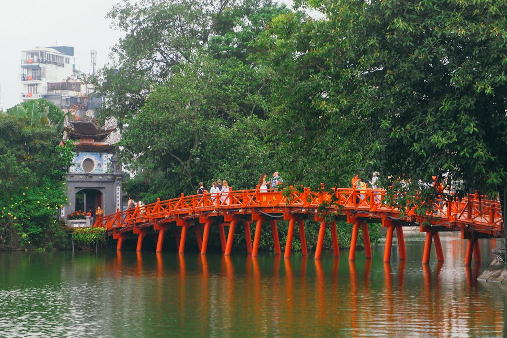 Stunning view of the iconic red bridge at Hoan Kiem Lake in Hanoi, Vietnam, surrounded by lush greenery.