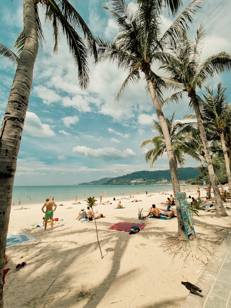 Sunny day at Patong Beach, Phuket, Thailand, featuring palm trees, sand, and relaxing tourists.