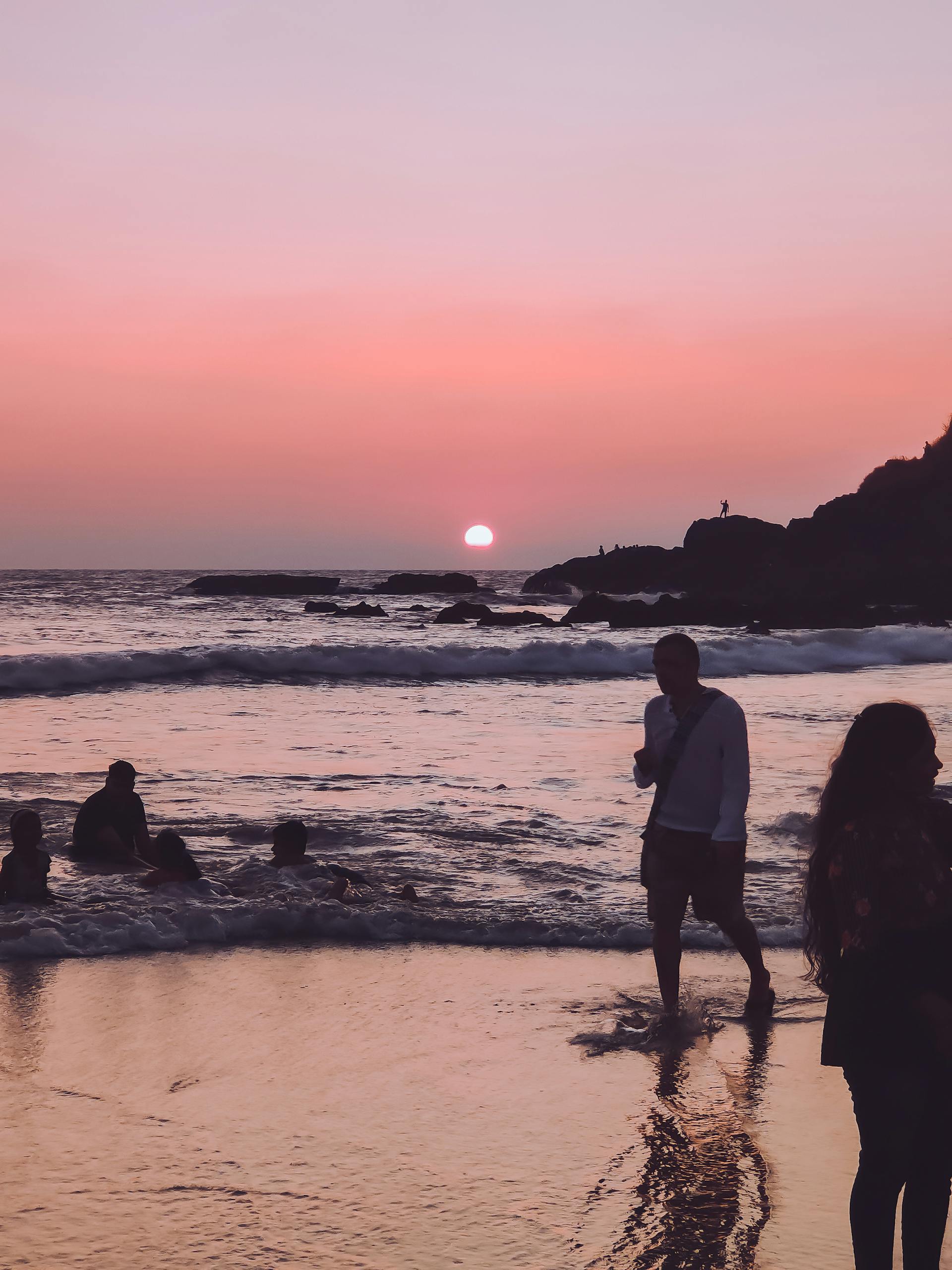 Beautiful sunset at Baga Beach, India with silhouettes of people enjoying the serene view.