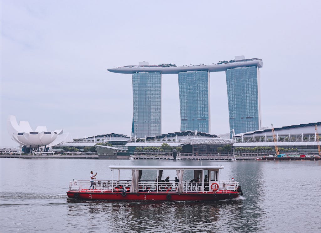 Scenic view of Marina Bay Sands and traditional riverboat in Singapore's urban harbor.