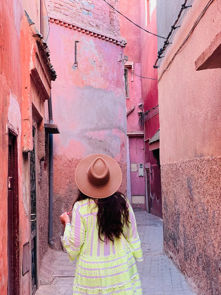 Woman in colorful dress explores the iconic pink alleys of Marrakech, Morocco.